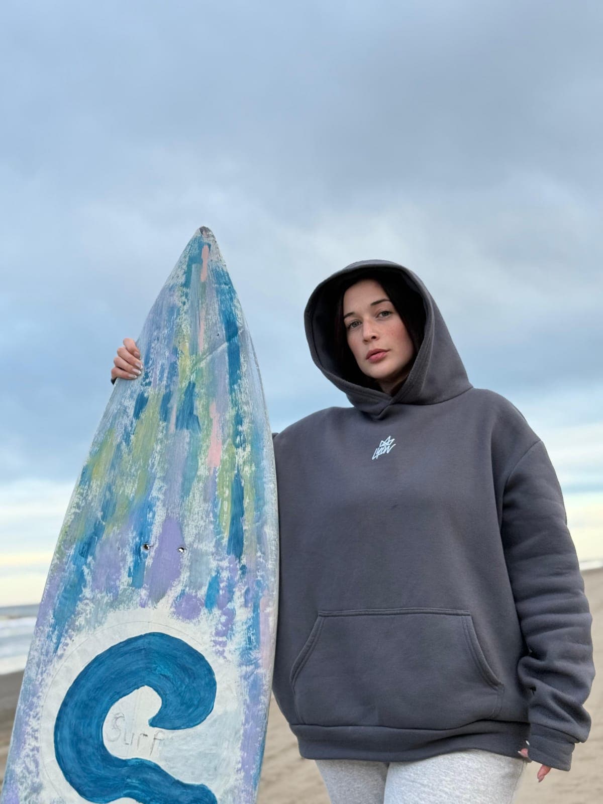 Persona con hoodie LYON junto a una tabla de surf pintada