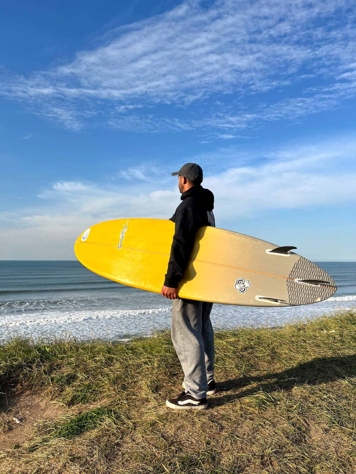 Persona con tabla de surf en la costa usando ropa LYON